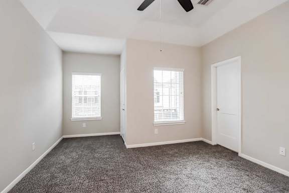 A room with a ceiling fan and two windows.