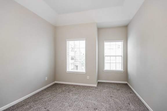 A room with two windows and carpeted floor.
