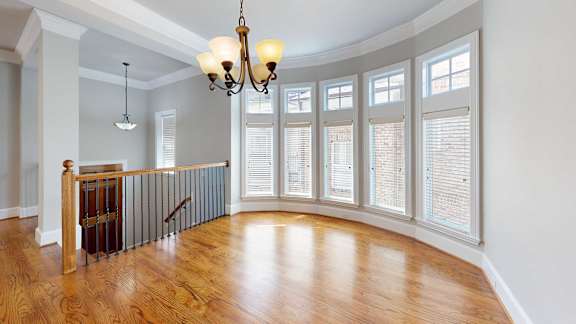 A chandelier hangs over a wooden floor in a room with a staircase.