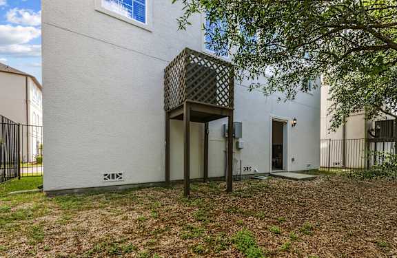 A white building with a black gate and a tree in front.