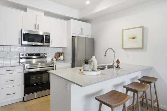A kitchen with white cabinets and a white island with a sink and three stools.