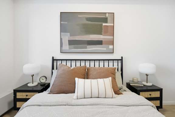 A bed with a white pillow and a painting on the wall.