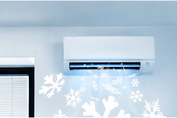 An air conditioner is on the wall with snowflakes coming out of it.