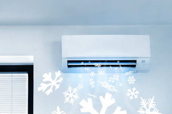 An air conditioner is on the wall with snowflakes coming out of it.