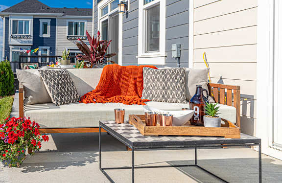 A grey couch with a pillow and a blanket on it is on a patio.