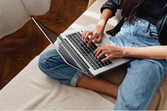 A person is sitting cross-legged on a white couch using a laptop.