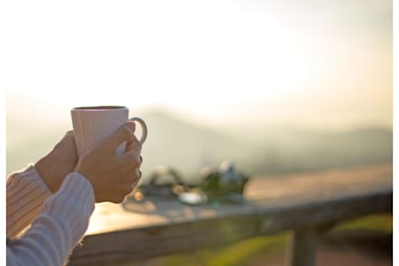 A person is holding a cup of coffee on a wooden bench.