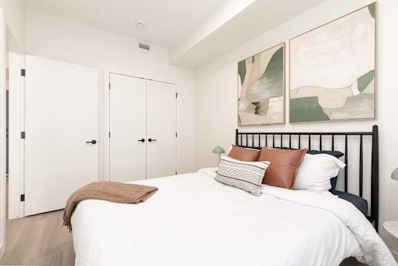 A bedroom with a bed, pillows, and a painting on the wall.