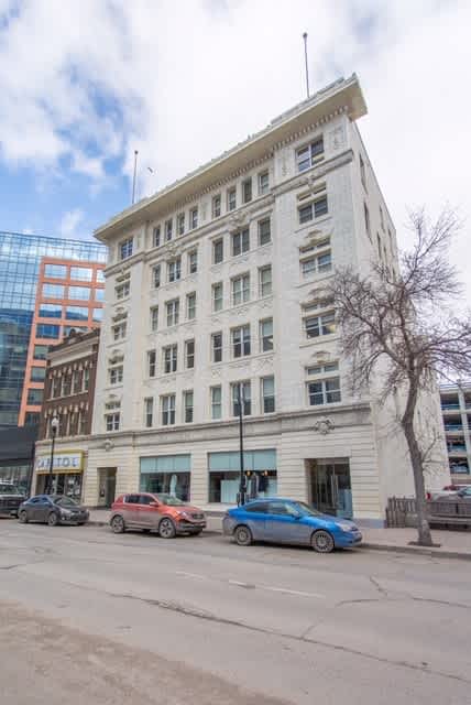A white building with a blue car parked in front of it.