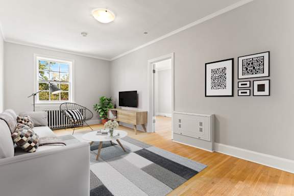 A living room with a grey couch, a coffee table, a plant, and a TV.