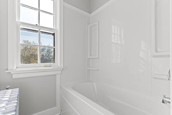 A white bathroom with a window and a bathtub.