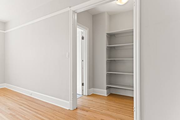 A white room with a wooden floor and a white closet with shelves.