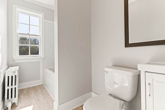 A white toilet sits next to a window in a bathroom.