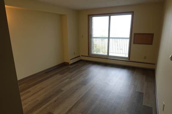 A room with wooden floors and a window with a view of a fence.