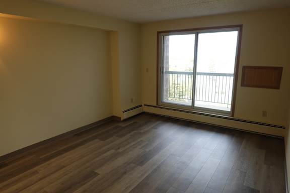 A room with wooden floors and a window overlooking a balcony.