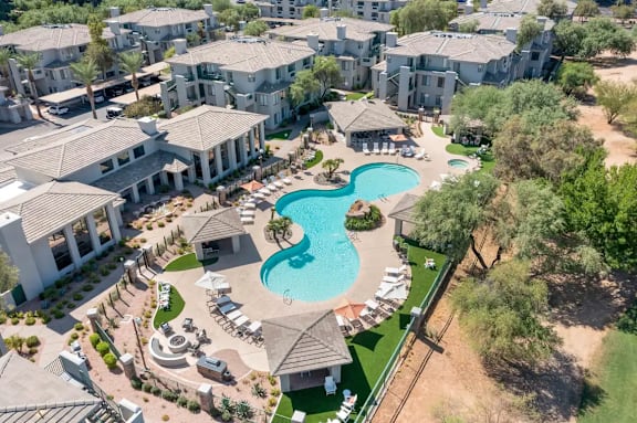 A large swimming pool surrounded by lounge chairs and umbrellas is the centerpiece of a resort-style community.