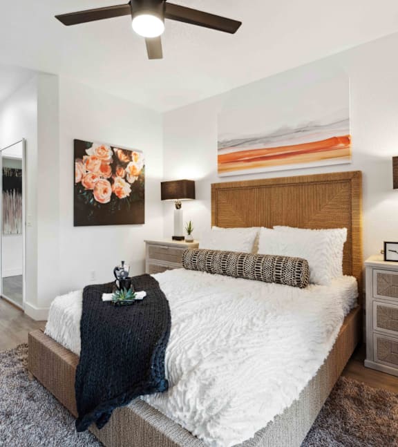 A bedroom with a bed, a ceiling fan, and a painting on the wall.