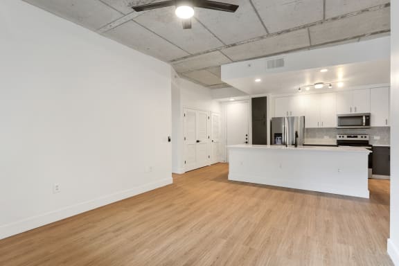 the living room and kitchen of an apartment with white walls and wood flooring
