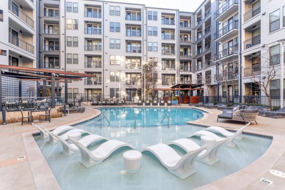 an apartment swimming pool with chaise lounge chairs in front of an apartment building