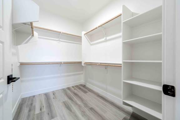 A walk-in closet with white shelving and a wooden floor.