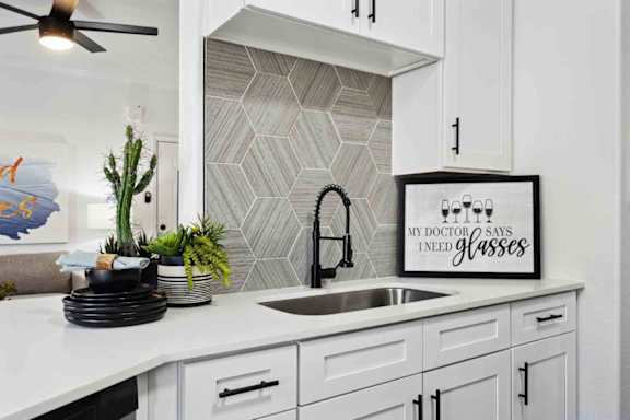 A kitchen with a white countertop and a framed sign that says "My doctor says I need glasses.".