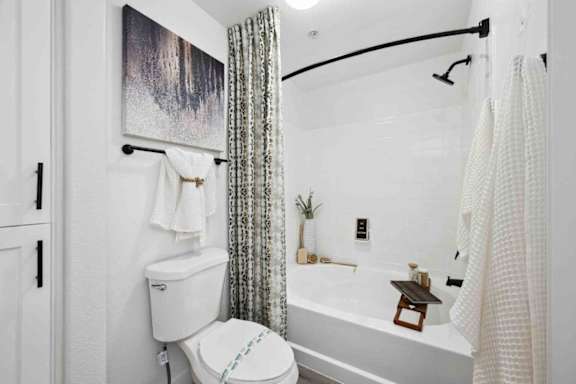 A white bathroom with a toilet, a bathtub, and a shower curtain.