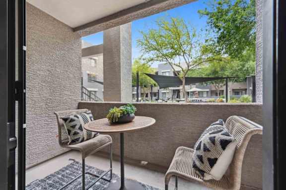A patio with a table, two chairs, and a potted plant.