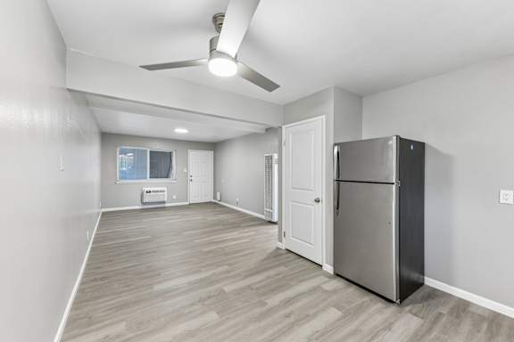 A spacious room with a refrigerator and a ceiling fan.