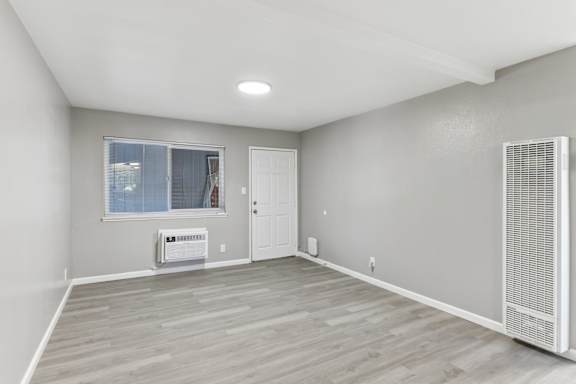 A living room with a window, a door, and a wall-mounted air conditioner unit.