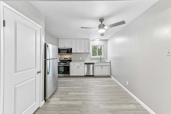 A kitchen with white cabinets and a stainless steel refrigerator, dishwasher, stove, and microwave. Ceiling fan over dining area, vinyl plank flooring, and window above the kitchen sink.