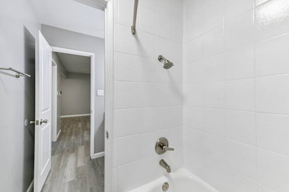 Bathroom with tub/shower with white tile walls, curved shower curtain rod, and towel bar.