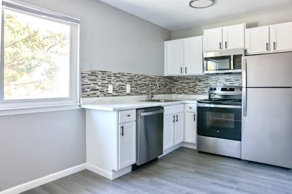 A kitchen with white cabinets and stainless steel appliances. Large window in kitchen area.