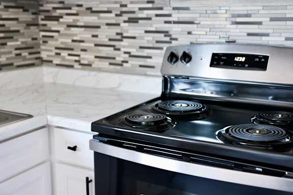 A stainless steel stove/oven with a digital display is in a kitchen with a marble looking counter.