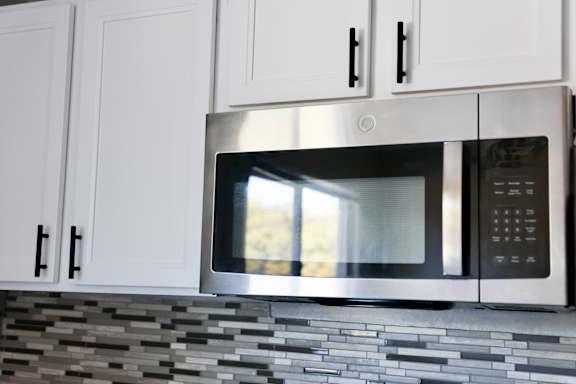 A stainless steel microwave oven is installed above a tiled backsplash in a kitchen.