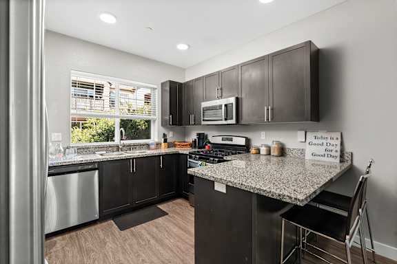 Kitchen with stainless steel appliances, granite counter tops, microwave mounted above stove, window above sink, two barstools at counter, and espresso colored cabinets.