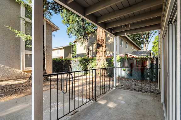 Covered patio overlooking fenced yard with large tree at Redwood Cove Apartments, Chico