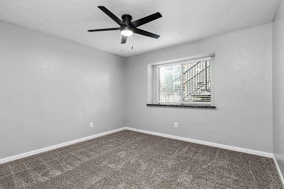Empty carpeted bedroom with ceiling fan and window at Redwood Cove Apartments, Chico, CA