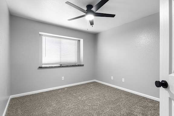 Empty carpeted bedroom with ceiling fan and blinds at Redwood Cove Apartments, Chico, California