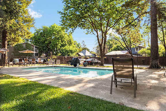 Outdoor pool area with lounge chairs and tree shade at Redwood Cove Apartments, California, 95928
