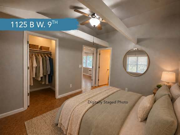 A bedroom with a bed, pillows, a ceiling fan, and a closet with clothes.