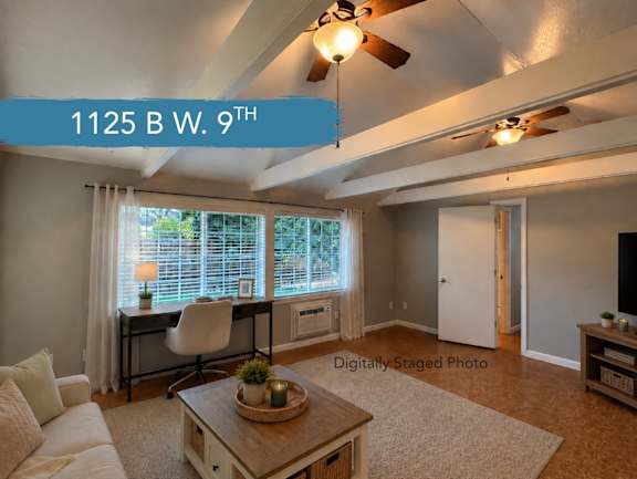 A living room with a white couch, a desk with a chair, and a ceiling fan.