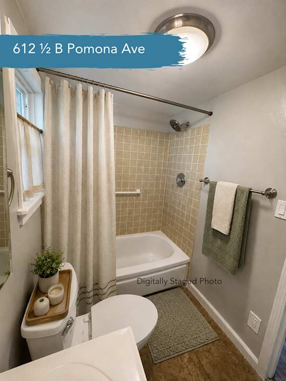 A bathroom with a white toilet, a white bathtub, a white sink, a white shower curtain, a green towel, and a brown tray with a plant and two bowls on it.