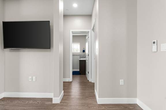 Flat screen TV mounted on left side of hall. Hallway leading from the living area to the downstairs bedroom, bathroom, and laundry.