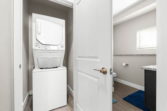 A white, stacked washer/dryer set in a closet next to the downstairs bathroom.