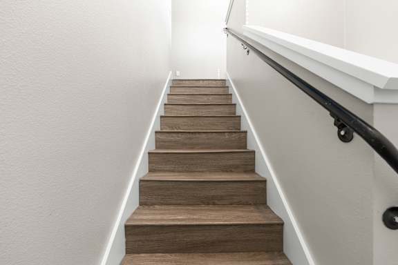 A staircase with vinyl plank steps and a black handrail going to second floor.