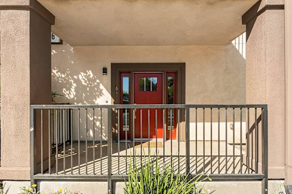 Front porch of apartment with red door, door length window on each side of door.