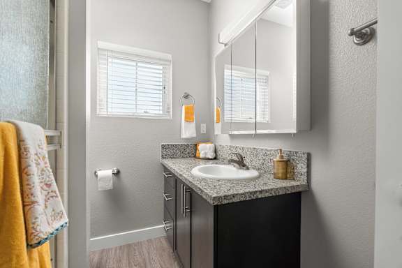 Main bedroom's private bathroom. Shower on right with frosted glass shower doors, granite vanity with single basin sink. Tri-fold medicine cabinet mirror, window left of bathroom vanity with faux wood blinds. Vinyl plan floors.