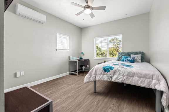 Third bedroom suite upstairs. Vinyl plank floors, ceiling fan and mini-split HVAC system in room. Full size bed,  one double window  directly across from bedroom door, and a smaller single window on the left side of the room from the entry door. Desk with a chair and side table. Flat screen TV mounted on wall opposite of double window.