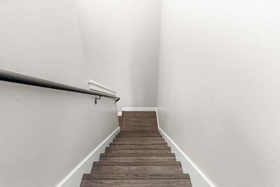 Stairs going down to the main floor. Vinyl plank treads and metal handrail.