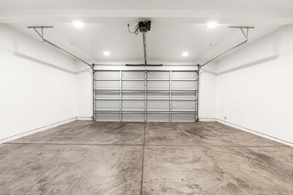 Single car garage with automatic rolling door, concrete floor, and white walls.